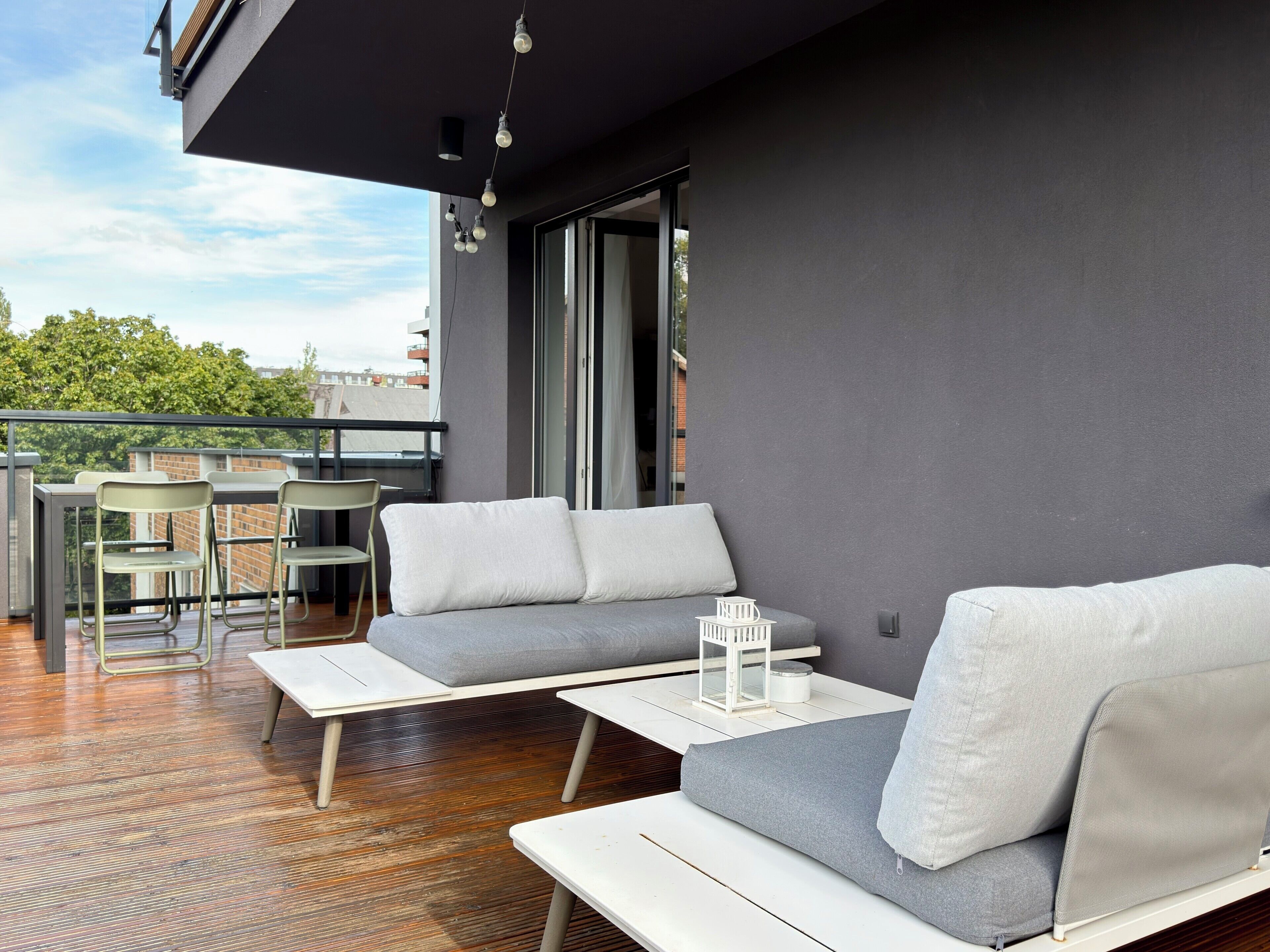 A modern outdoor seating area with a sofa and chairs, a small table, and a decorative lantern.