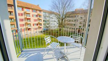 Un balcon avec une table en métal et deux chaises, donnant sur un espace verdoyant et des immeubles.