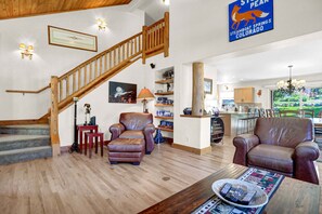 A spacious living area with a wooden staircase, leather sofas, a coffee table, and a kitchen in the background. - Duplex in Family Neighborhood - Easy Parking - On Ski Bus Line (Steamboat Springs)