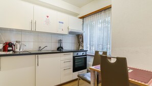 Uma cozinha compacta com armários brancos, fogão e pia. Há uma mesa de jantar com cadeiras.