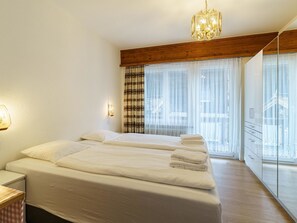 Ett hotellrum med en stor säng, ett nattduksbord, en kristallkrona och utsikt över omgivningarna genom tunna, genomskinliga gardiner.