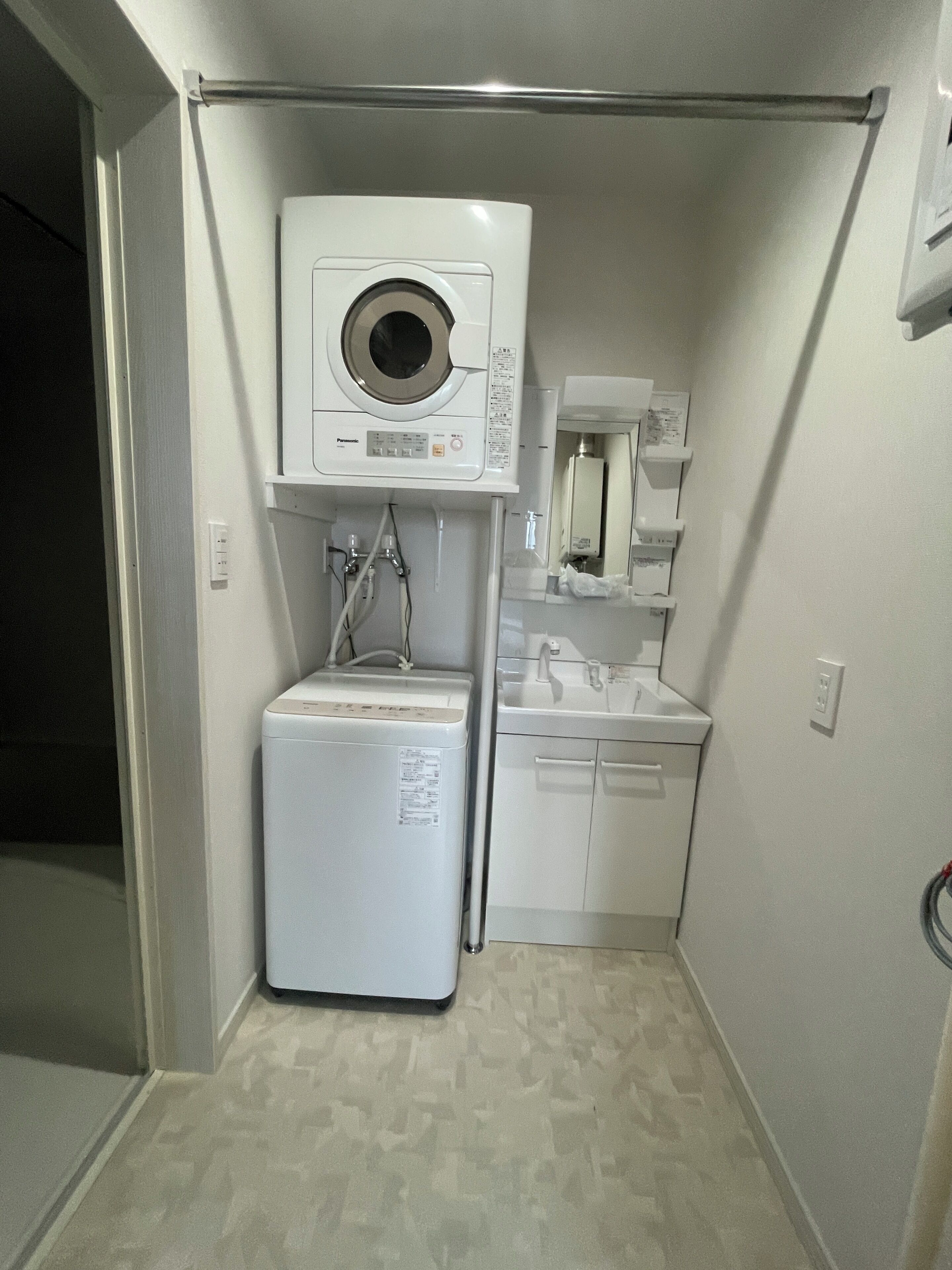 Een kleine wasruimte met een voorlader wasmachine en droger, een klein wasbakje en een spiegel boven de wasbak.