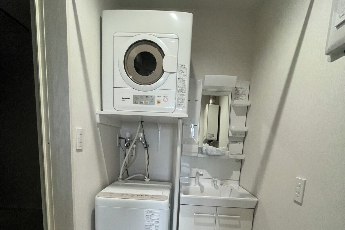 A compact laundry room with a front-loading washer and dryer, a small sink, and a mirror above the sink.