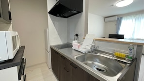 A modern kitchen with a stainless steel sink, a microwave, and a black range hood. - Casa Biei (Biei)