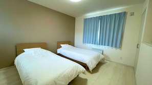 A room with two single beds, a window with curtains, and a radiator. - Casa Biei (Biei)
