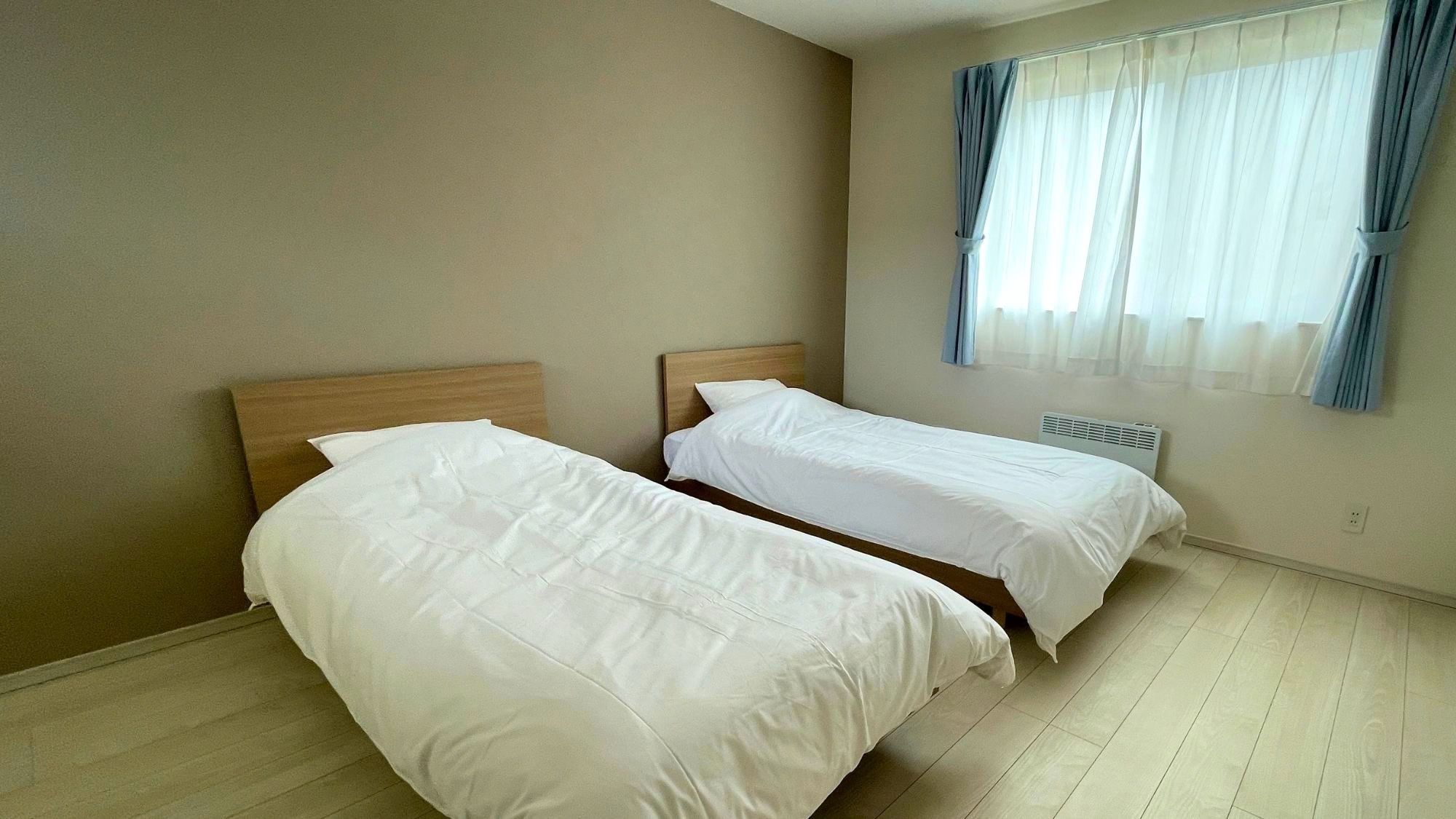 A room with two single beds, a window with curtains, and a radiator.