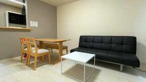 A small living area with a wooden table, a black sofa, and a single chair. - Casa Biei (Biei)