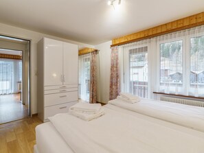 Ein Hotelzimmer mit zwei Betten, einem Kleiderschrank und großen Fenstern mit Vorhängen.