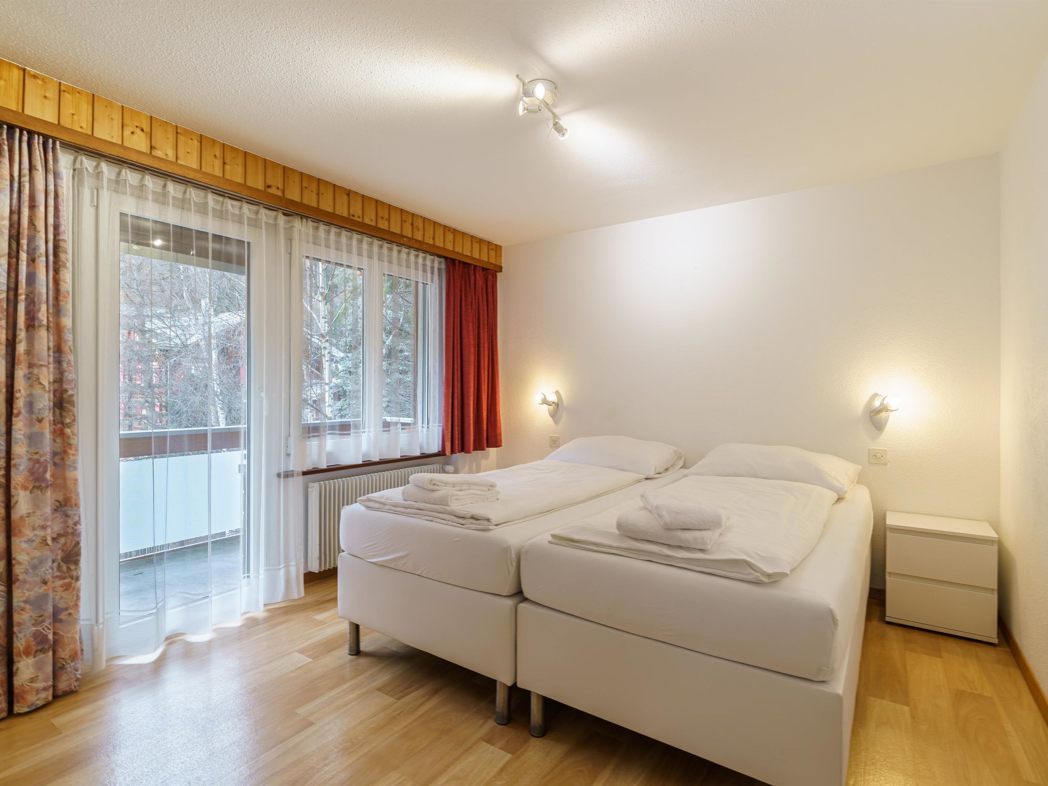 Une chambre d’hôtel avec un lit double, deux tables de chevet, une fenêtre avec des rideaux et une vue sur les arbres à l’extérieur.
