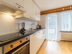 Eine moderne Küche mit Herd, Backofen und Spüle, Holzboden und einem Fenster mit transparenten Vorhängen.