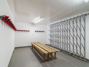 Ein Zimmer mit einer hölzernen Bank, einem roten und schwarzen Kleiderständer und einem grauen Metallregal mit Haken.