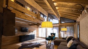 Ein gemütliches Blockhaus-Interieur mit Holzbalkendecke, einer Couch, einem Fernseher und einem Lederteppich.