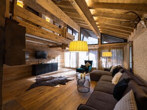 Ein gemütliches Blockhaus-Interieur mit Holzbalkendecke, einer Couch, einem Fernseher und einem Lederteppich.
