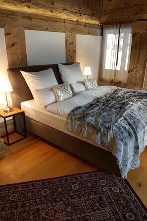 A bed with a patterned blanket, a bedside lamp, and a patterned rug in a room with wooden walls and a sloped ceiling. - Villa Alpenhof by Interhome (Saas-Almagell)