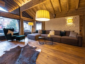 A cozy room with a wooden ceiling, a large sofa, a chair, a small table with candles, and a fur rug. - Villa Alpenhof by Interhome (Saas-Almagell)