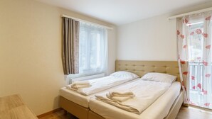 A hotel room with a double bed, a window with curtains, a bedside table, and a wooden floor. - Haus Astoria by Interhome (Saas-Grund)