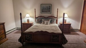 Ein Himmelbett mit einer Steppdecke, zwei Nachttischlampen, ein Nachttisch und ein an der Wand hängendes Gemälde.
