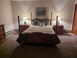 Ein Himmelbett mit einer Steppdecke, zwei Nachttischlampen, ein Nachttisch und ein an der Wand hängendes Gemälde.