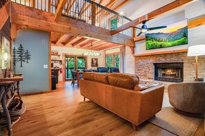 A spacious living room with a fireplace, wooden floors, and a high ceiling with exposed beams. - The Smoky Edit | 3 Decks | Hot Tub | Pool Table | 2 Fire Pits (Gatlinburg)