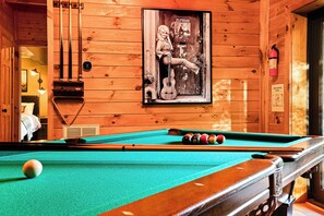 Une table de billard avec des billes, une queue et une affiche encadrée accrochée au mur.