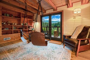 A cozy cabin interior with a hanging chair, wooden shelves, and a view through a glass door. - The Smoky Edit | 3 Decks | Hot Tub | Pool Table | 2 Fire Pits (Gatlinburg)