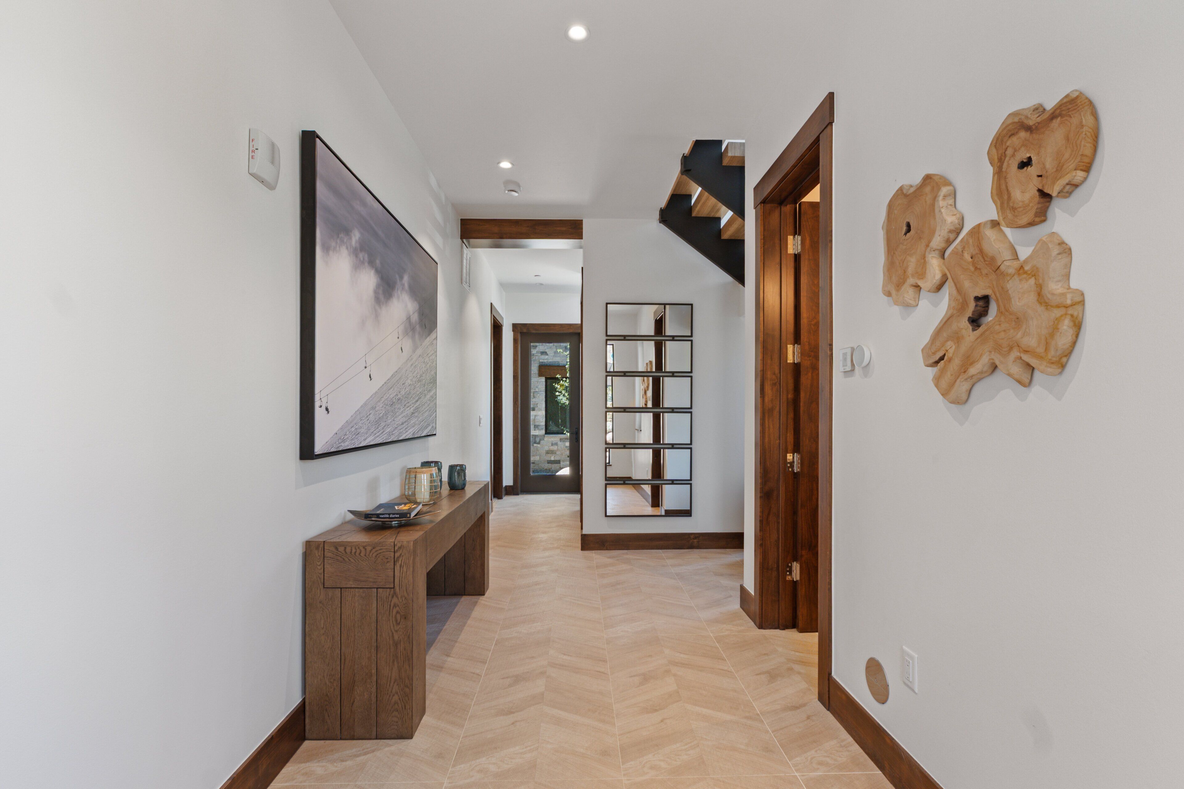 Un pasillo con una consola de madera, una obra de arte enmarcadas y un conjunto de adornos de madera en la pared.