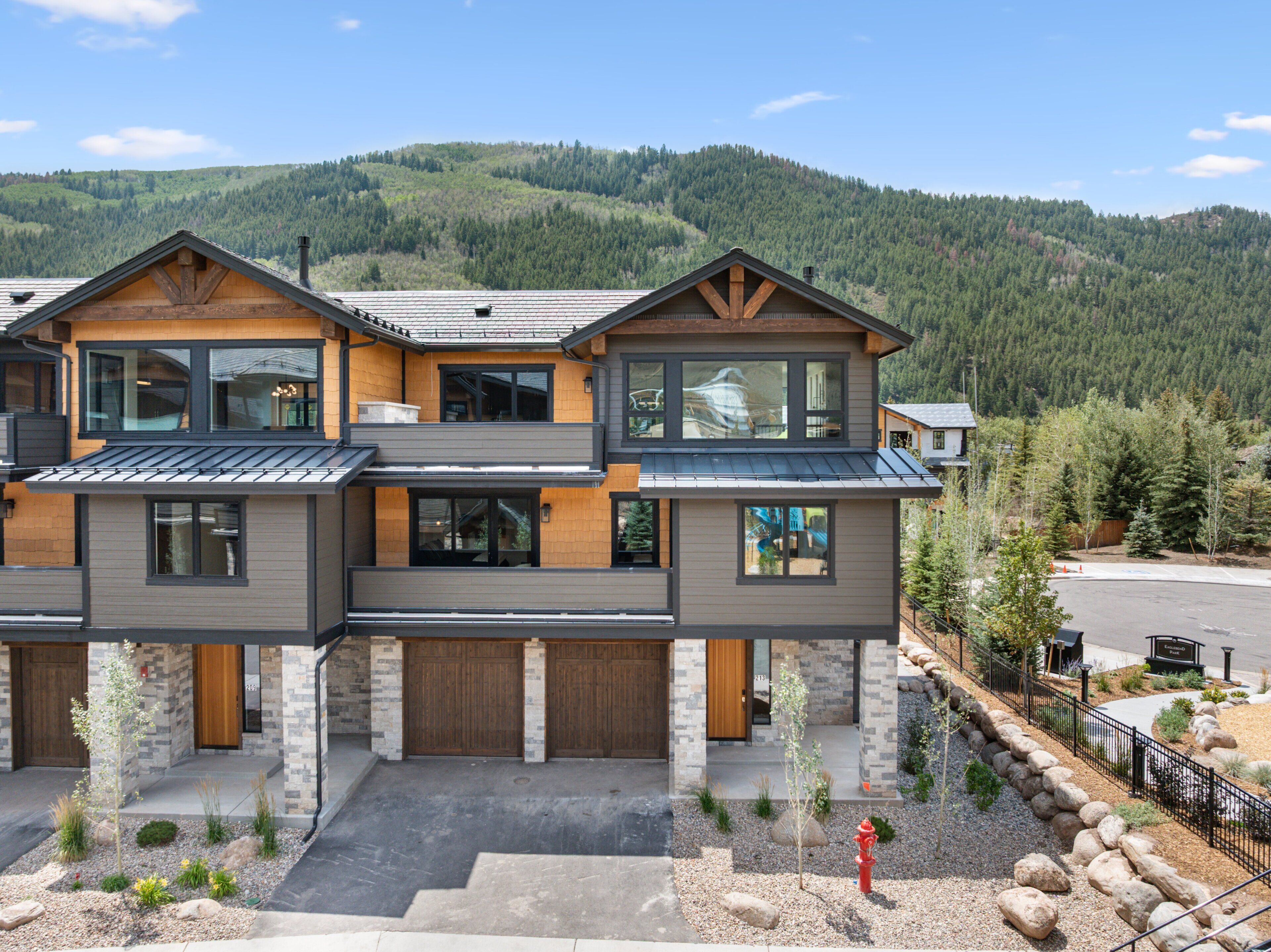 A modern two-story house with a garage, large windows, and a view of a forested mountain.