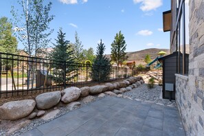A paved patio area with a stone wall and a metal fence. - Mountain-view Avon townhome with 3 bedrooms, hot tub, fireplace, and deck. (Avon)