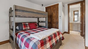 A bunk bed with a plaid bedspread, a wooden wardrobe, and a bathroom visible through an open door. - Mountain-view Avon townhome with 3 bedrooms, hot tub, fireplace, and deck. (Avon)
