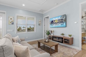 Una sala de estar con sofá, mesa de centro y televisor mostrando un anuncio de vacaciones.