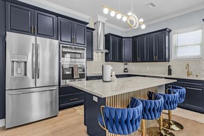 Una cocina moderna con armarios oscuros, electrodomésticos de acero inoxidable, una isla de mármol y taburetes de bar azules.