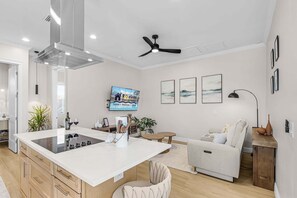 A modern kitchen with an island, a dining area with a sofa, and a flat-screen TV mounted on the wall. - Poolside Fun, Pickleball & Coastal Adventures Await in Fort Myers - Jefferson Palms 123 - Roelens (Fort Myers Beach)