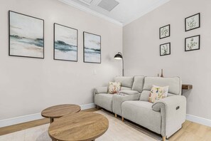 A living room with a grey sofa, two round wooden tables, and wall-mounted artwork. - Poolside Fun, Pickleball & Coastal Adventures Await in Fort Myers - Jefferson Palms 123 - Roelens (Fort Myers Beach)
