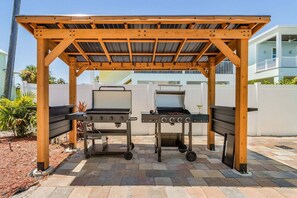 A covered outdoor grilling area with two barbecue grills, a pergola structure, and a paved patio. - Poolside Fun, Pickleball & Coastal Adventures Await in Fort Myers - Jefferson Palms 123 - Roelens (Fort Myers Beach)