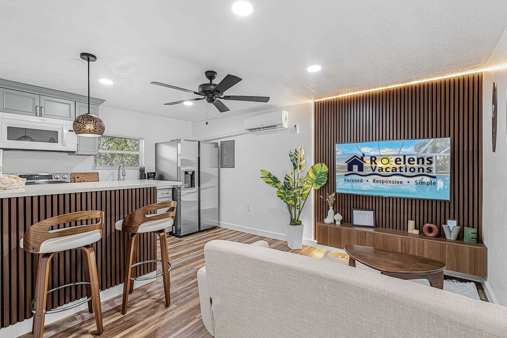 Uma cozinha moderna com micro-ondas, frigorífico e zona de refeições com um banco alto e um sofá.