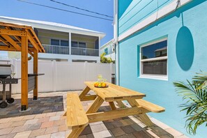 A wooden picnic table with a bench, a grill, and a white fence in a backyard. - Poolside Fun, Pickleball & Coastal Adventures Await in Fort Myers - Jefferson Palms 125-7a - Roelens (Fort Myers Beach)