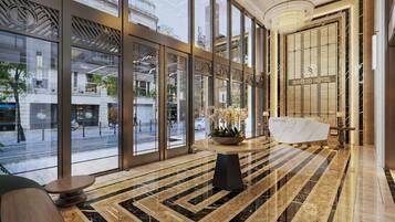 Un vestíbulo de hotel con ventanas amplias, un mostrador de recepción de mármol y una lámpara de araña moderna.