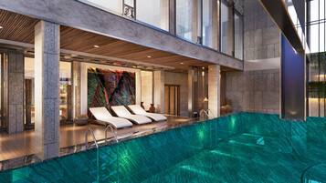 Piscina interior moderna con sillones de descanso y una pared decorativa.