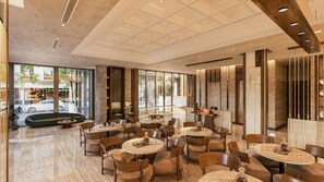 A modern interior with round tables and chairs, large windows, and a seating area with a bench. - VP Sisaked Hotel (Vientiane)