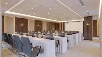 Un salón de conferencias con mesas largas, sillas y una pantalla para proyector.