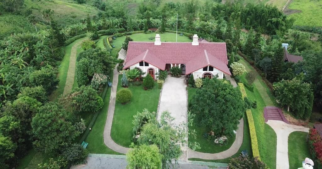 A large house with a red roof, surrounded by a well-maintained lawn and trees.