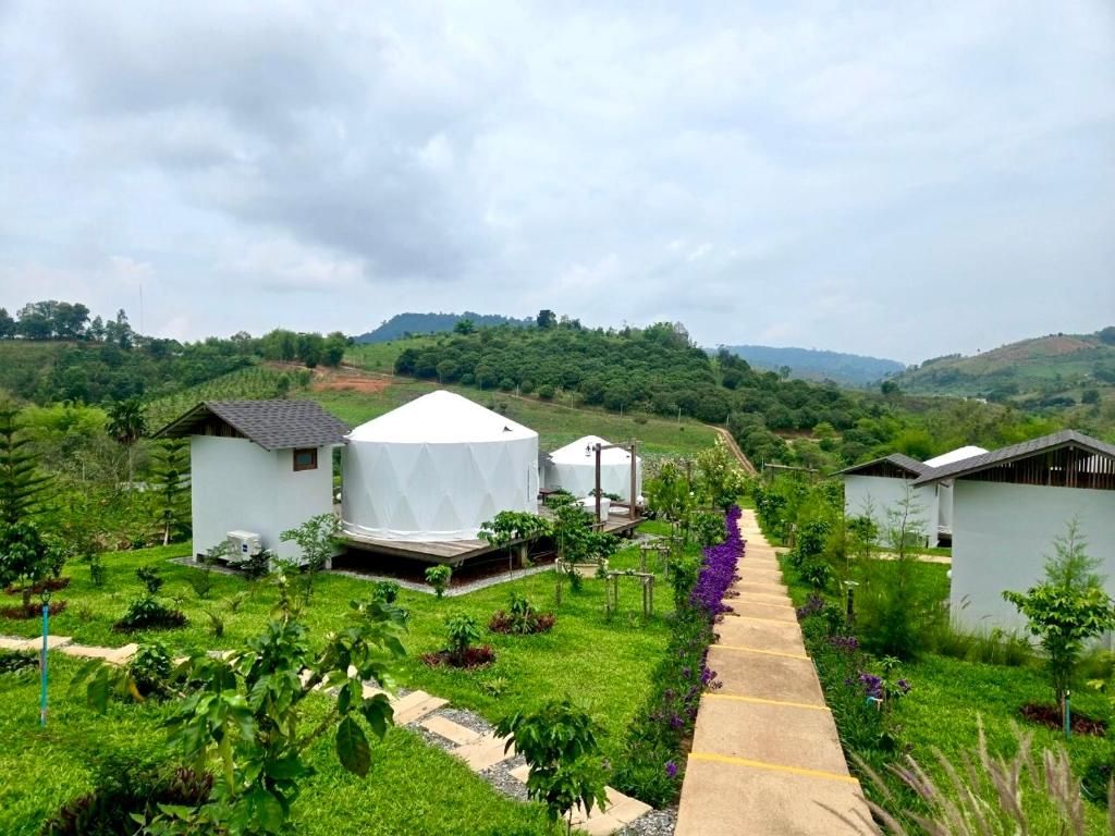 Un entorno rural con edificios blancos, un sendero en un jardín y colinas verdes al fondo.