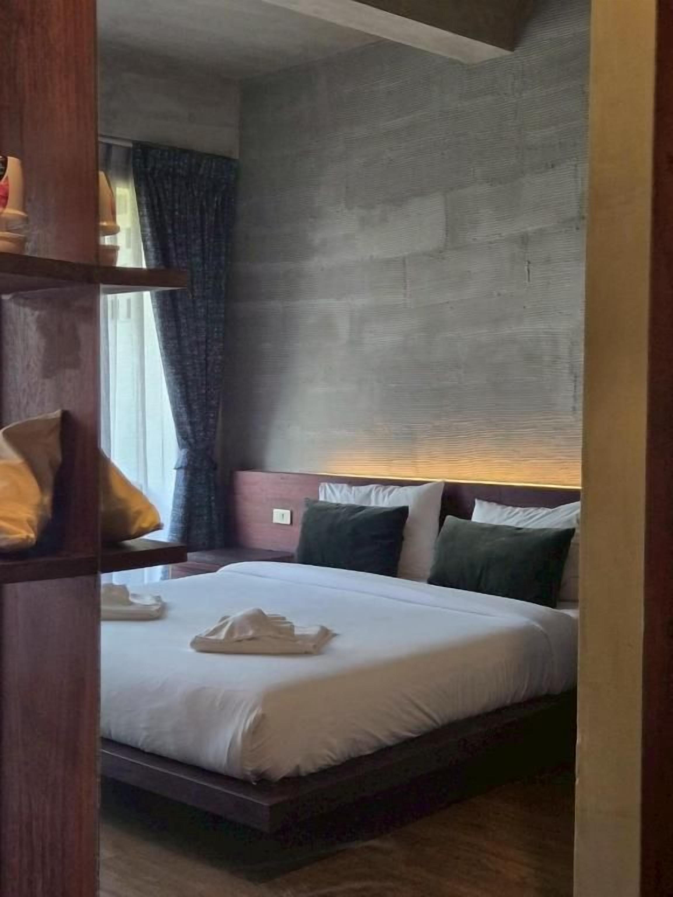 A hotel room with a bed, pillows, a wooden headboard, and a nightstand.