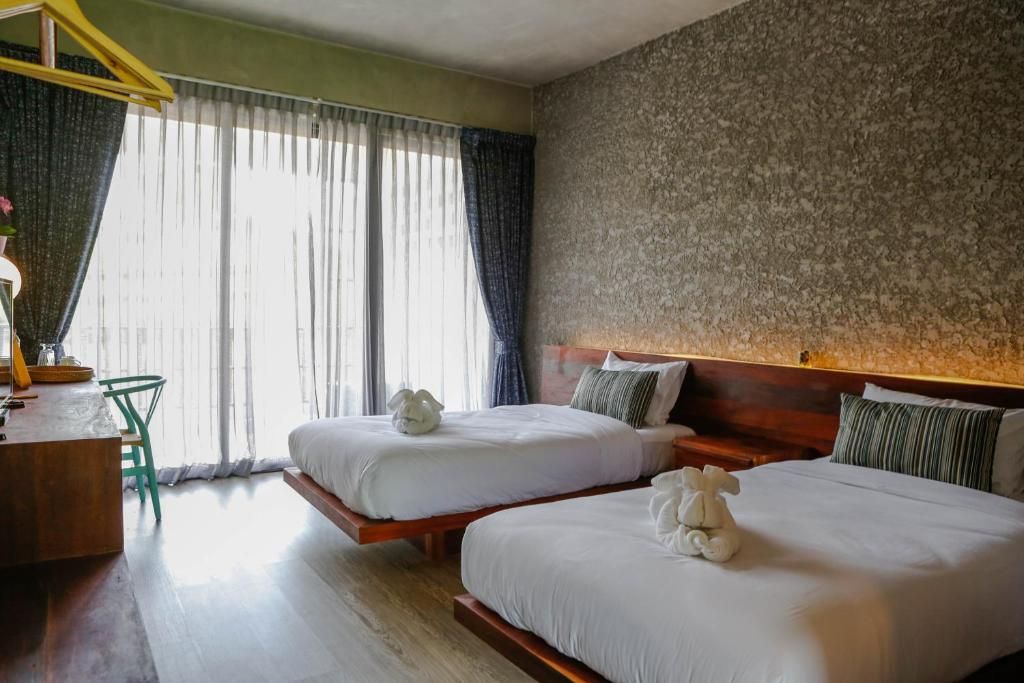 Habitación de hotel con dos camas, cabecero de madera, escritorio con silla y ventana con cortinas.