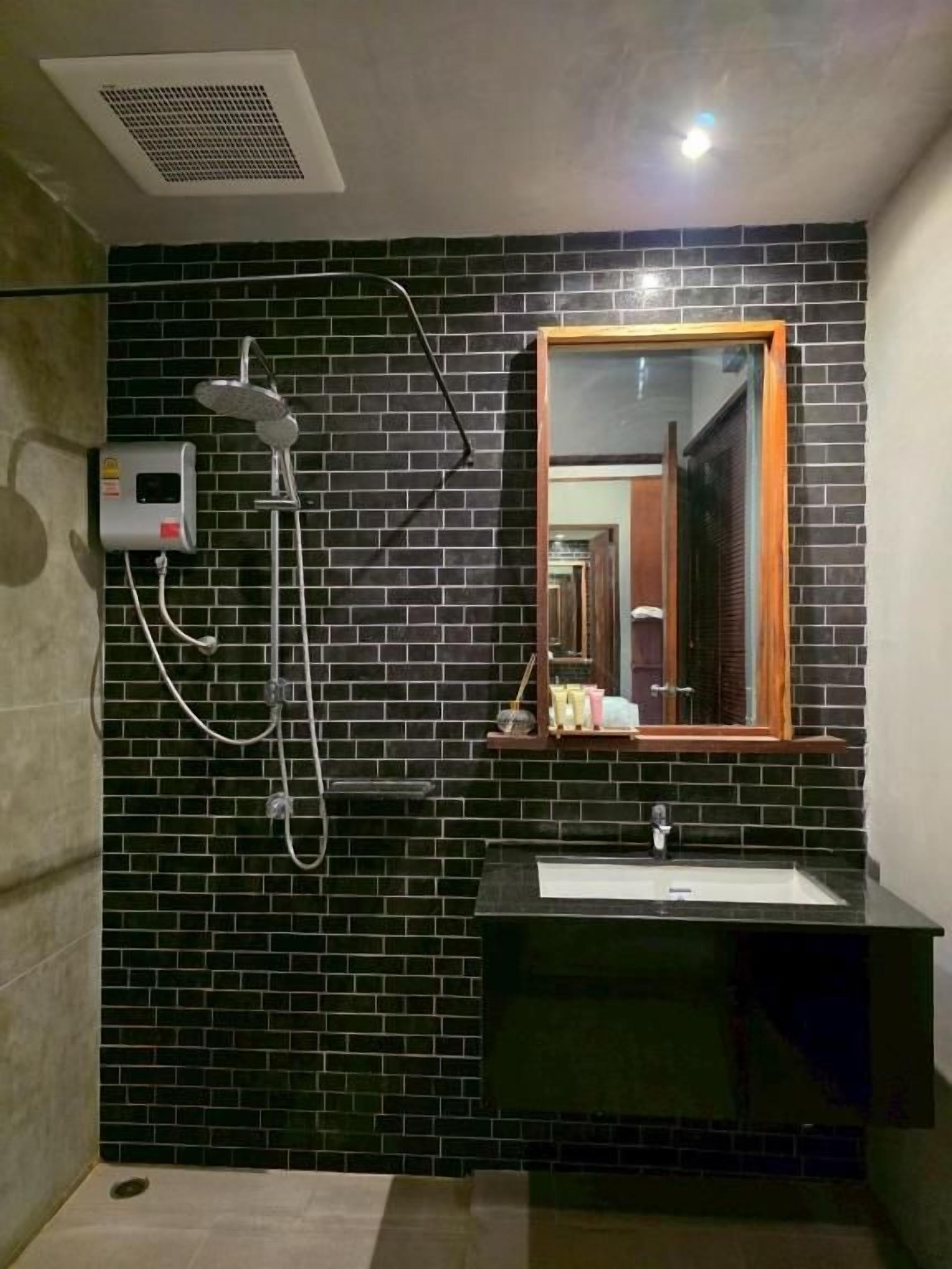 A bathroom with a black tiled wall, a shower, a sink, and a mirror.