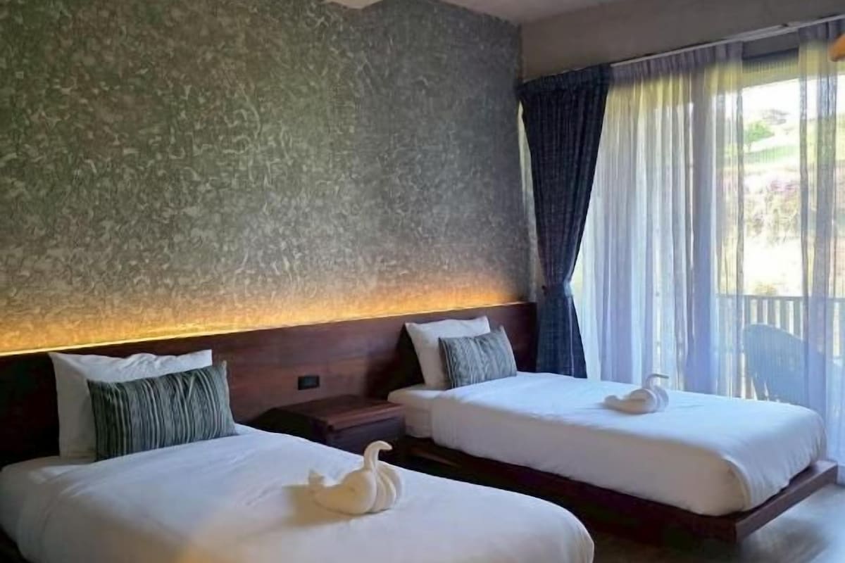 Hotellihuone, jossa on kaksi sänkyä, kuvioitu seinä, puulattia ja ikkuna, jossa on verhot.