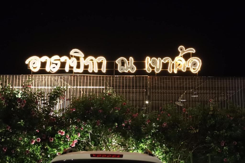 A sign with illuminated text, a fence, and flowering plants.