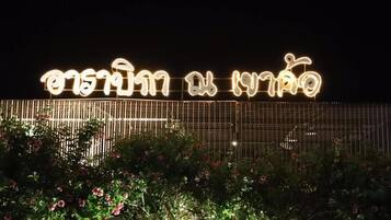 A sign with illuminated text, a fence, and flowering plants.