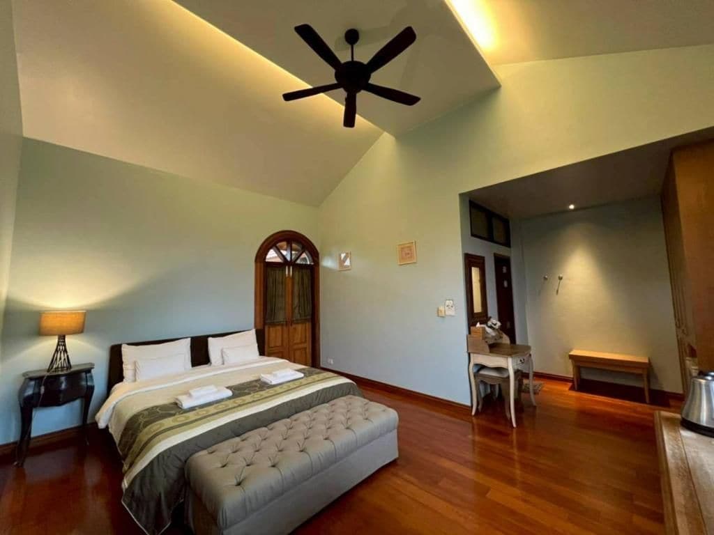 Un dormitorio con una cama, un escritorio, una silla, un banco y un ventilador de techo.