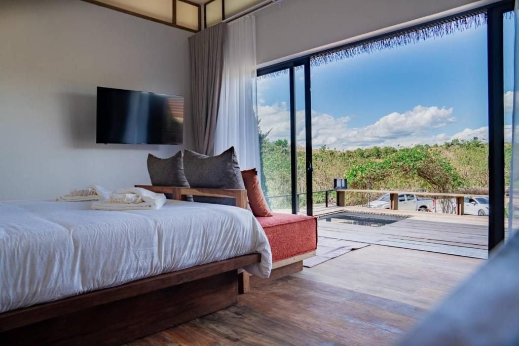 Un dormitorio con una cama grande, televisión de pantalla plana, vistas al exterior a través de una puerta corredera de vidrio y un balcón con terraza de madera.